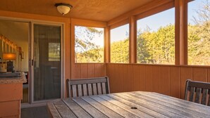 Une terrasse en bois avec une table et des chaises, une porte-fenêtre coulissante et une vue sur les arbres.
