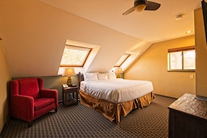 A hotel room with a bed, a red armchair, two bedside tables with lamps, and a ceiling fan.