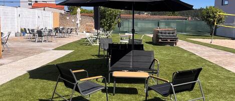 An outdoor seating area with a table and chairs under a large umbrella, surrounded by artificial grass.