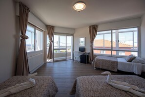 Een hotelkamer met twee bedden, een bureau, een computer en grote ramen met gordijnen.