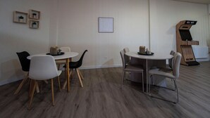 Una habitación con una mesa redonda y sillas, un cuadro enmarcado en la pared, y una estructura de madera con la etiqueta 'GLINT' a la derecha.
