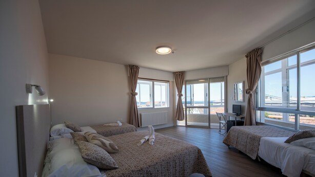 Habitación de hotel con dos camas, un escritorio con computadora y ventanas amplias con vista a un puente.
