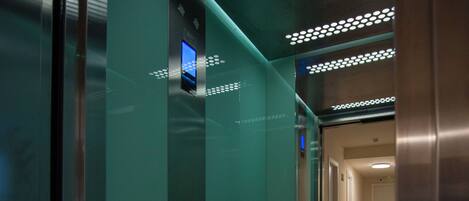 An elevator interior with a digital display, emergency buttons, and a metallic handrail.