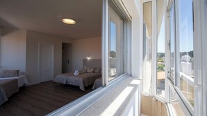 Un dormitorio con dos camas, un ventanal grande y una puerta que da a otra habitación.