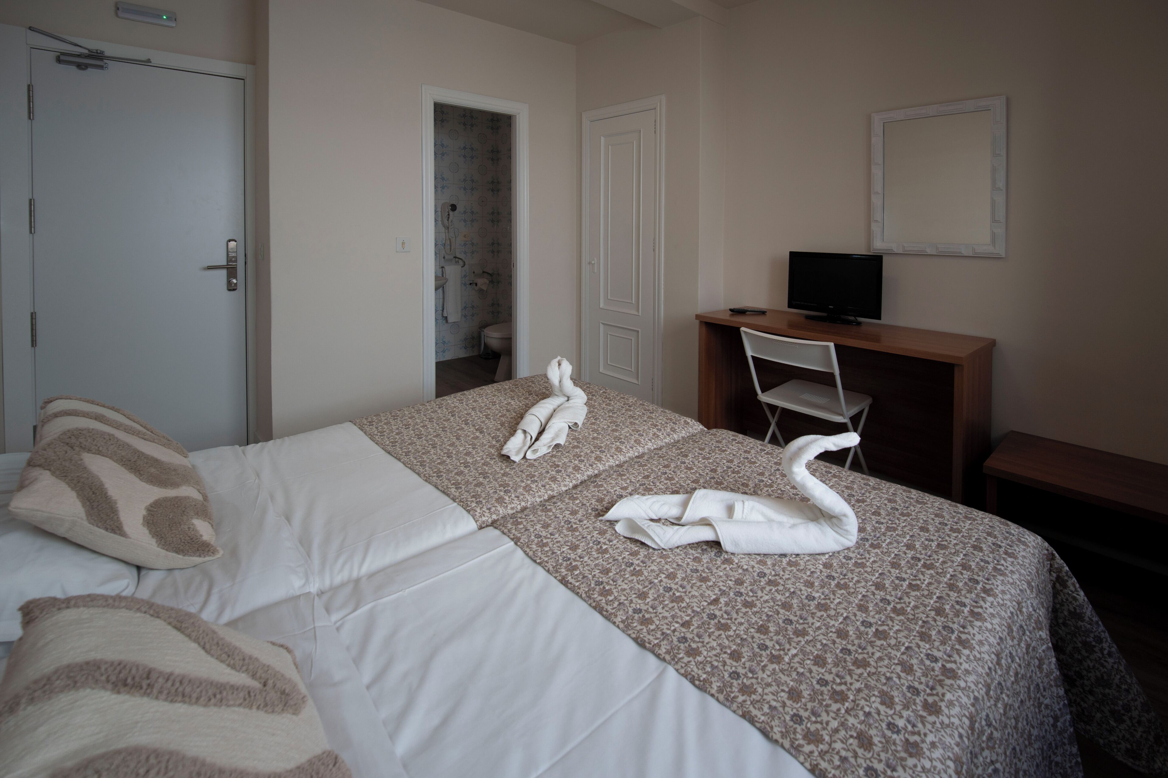 Habitación de hotel con cama, escritorio con televisor y baño visible a través de una puerta abierta.
