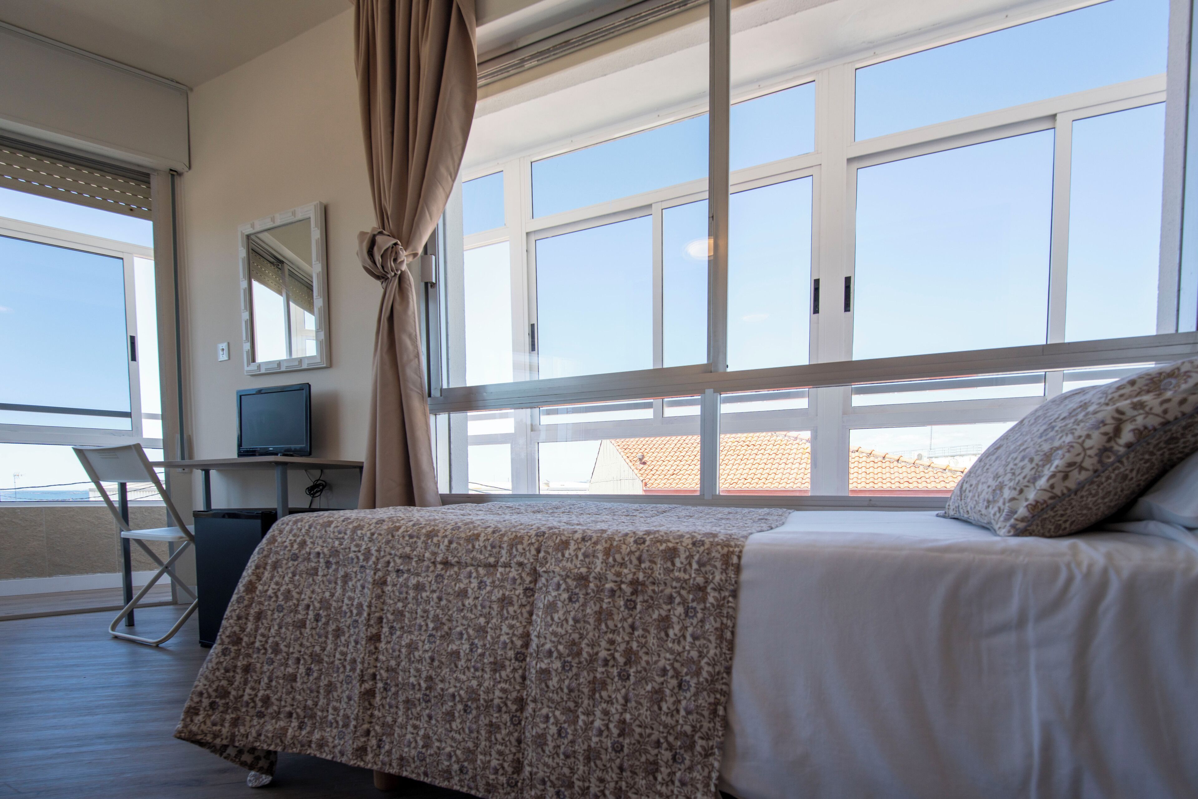 Une chambre d’hôtel avec un lit, un bureau avec une télévision, une chaise et de grandes fenêtres.