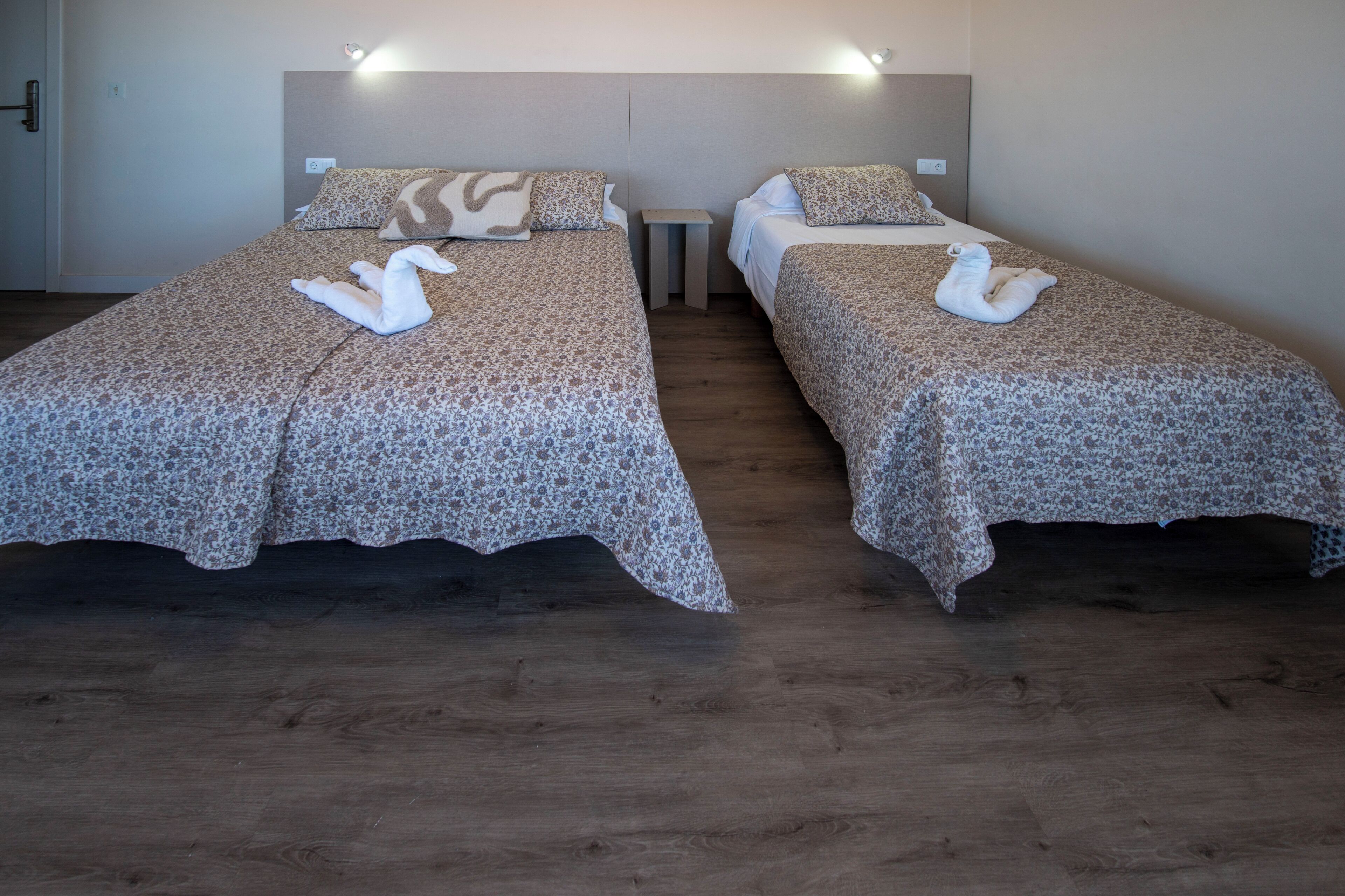 A hotel room with two single beds, each with a floral-patterned bedspread and a swan-shaped pillow.