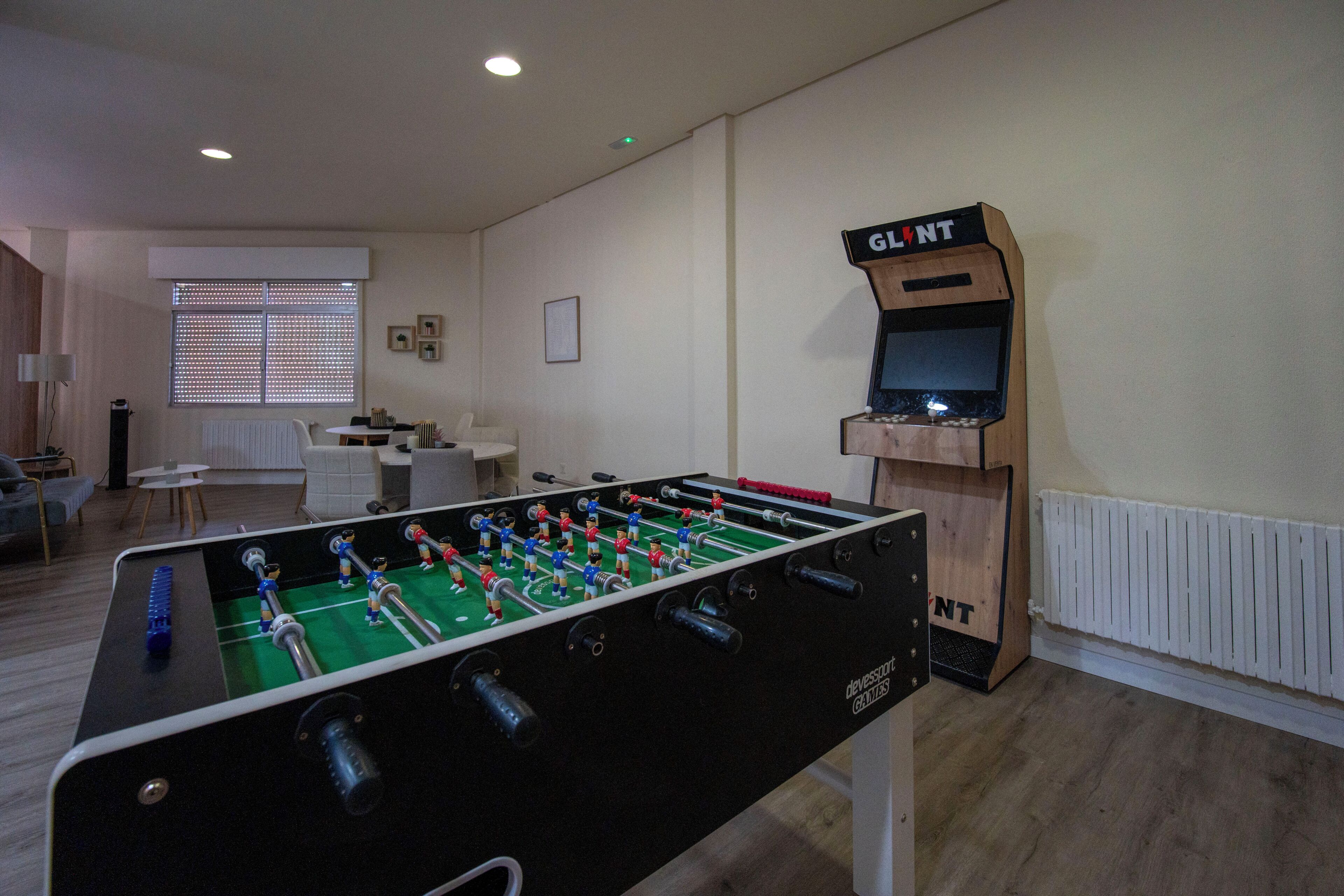 Une pièce avec une table de baby-foot, un petit écran de télévision et une fenêtre avec des stores.