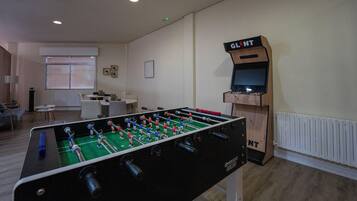 Une pièce avec une table de baby-foot, un petit écran de télévision et une fenêtre avec des stores.