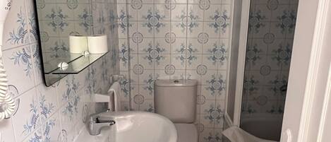 Un baño con lavamanos, inodoro y zona de ducha blancos.