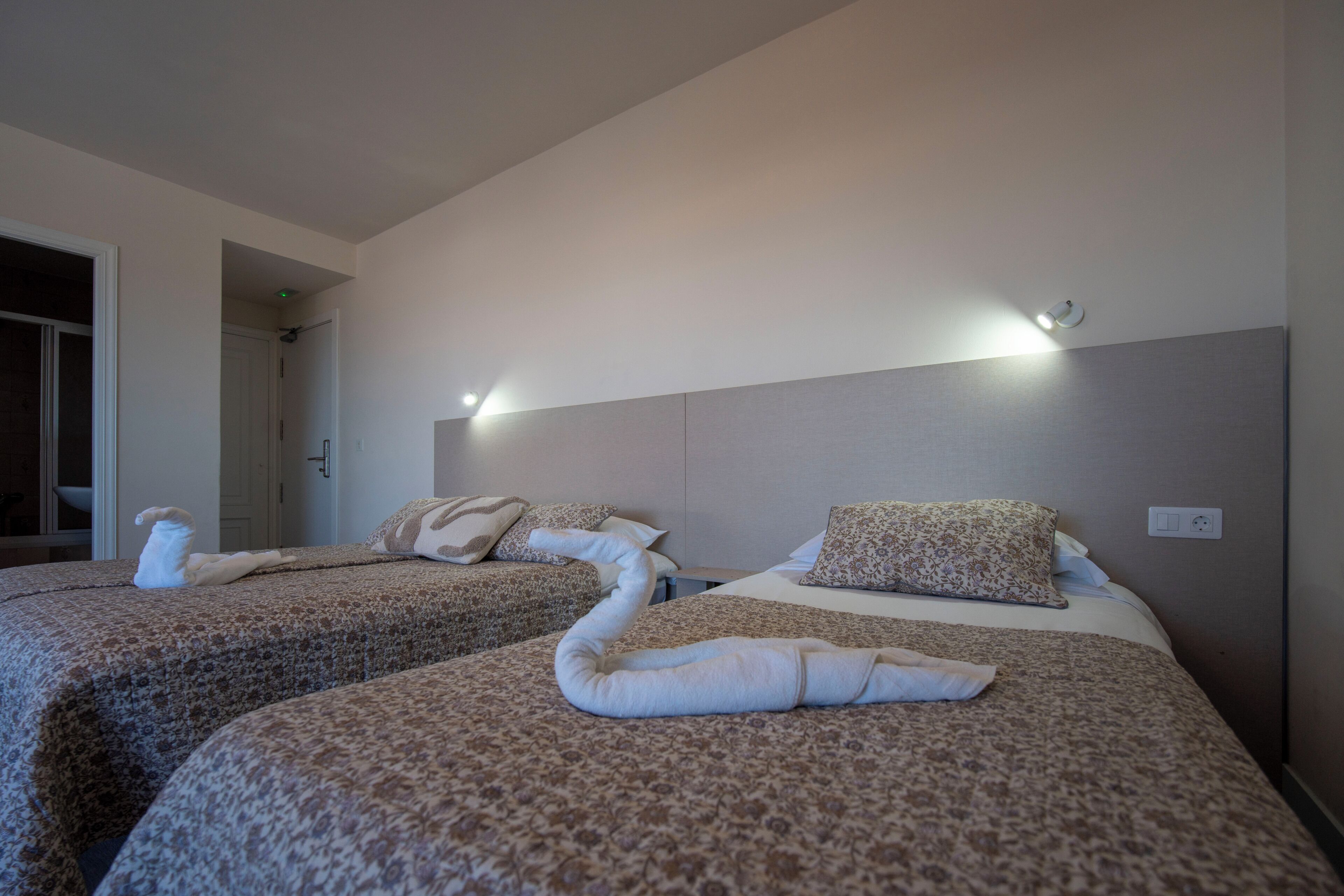 Een hotelkamer met twee bedden, elk voorzien van een bloemenprint deken en kussens, en een hoofdbord met ingebouwde verlichting.
