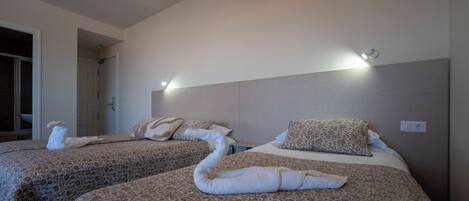 Habitación de hotel con dos camas, cada una con colcha y almohadas estampadas con motivos florales, y cabecera con iluminación integrada.