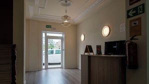 Un vestíbulo de hotel con una recepción, un techo con molduras decorativas y una puerta que da al exterior.