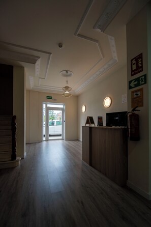 Een hotel lobby met een receptiebalie, een plafond met decoratieve ornaments, en een deur die naar buiten leidt.