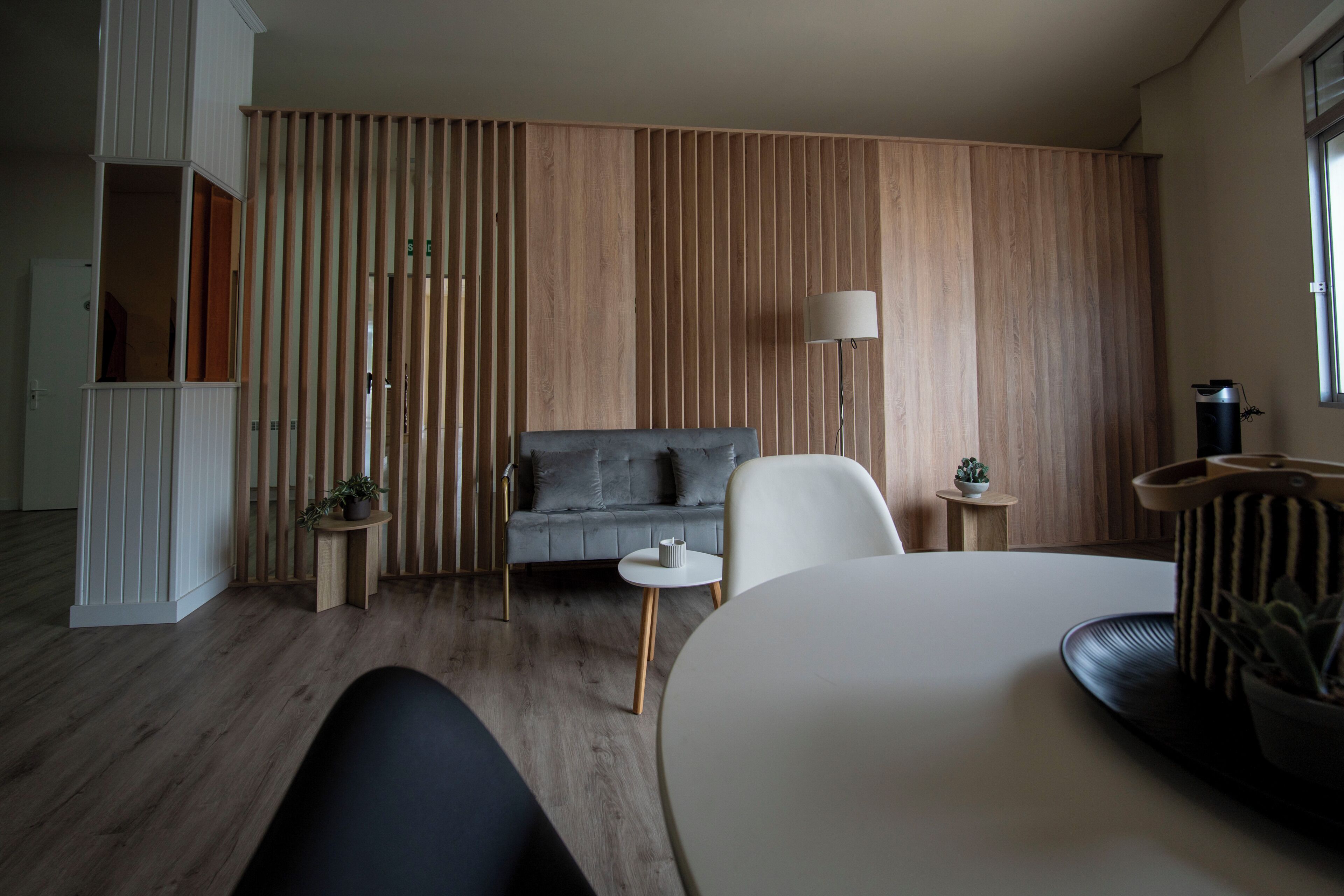 Una sala moderna con un sofá gris, un sillón blanco, una mesa de centro redonda y una mesita auxiliar con una planta.
