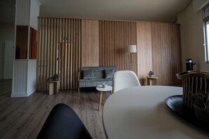 Una sala moderna con un sofá gris, un sillón blanco, una mesa de centro redonda y una mesita auxiliar con una planta.