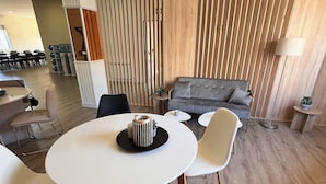 Una sala de estar moderna con un sofá gris, una mesa redonda blanca con dos sillas y un separador de madera con listones verticales.