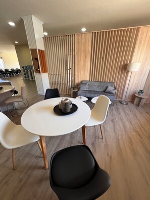Een moderne woonkamer met een grijze bank, een ronde witte tafel met twee stoelen, en een houten wand met verticale latten.