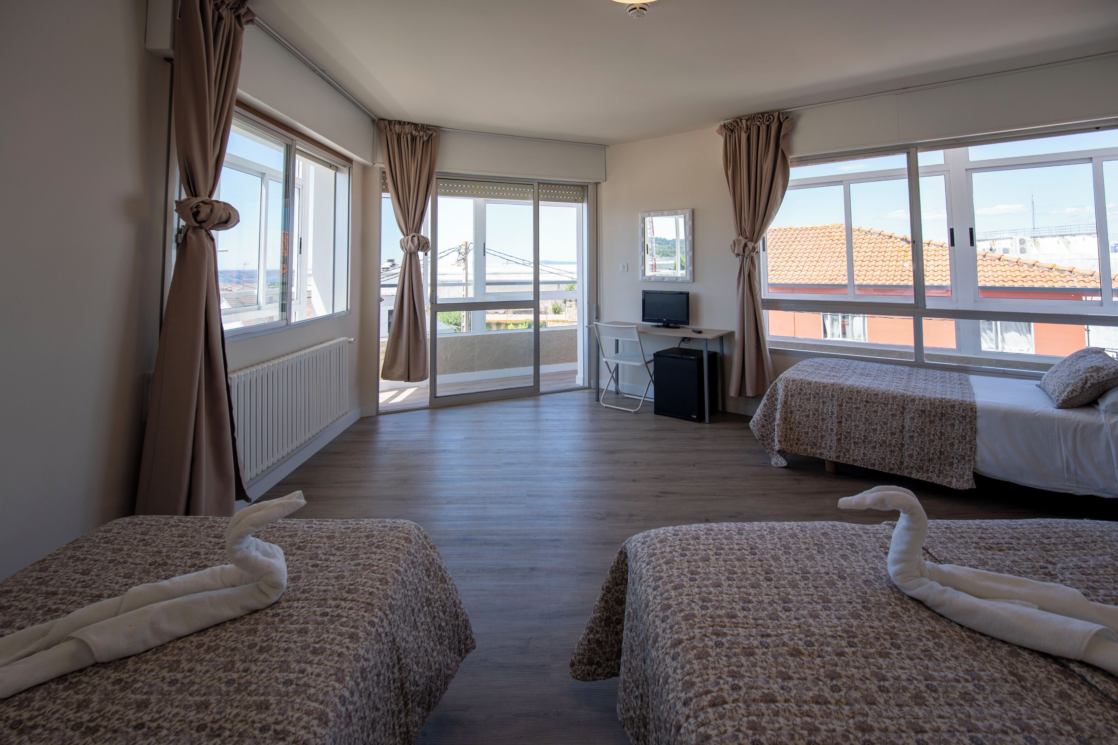 Quarto de hotel com duas camas, uma escrivaninha com computador e amplas janelas com vista para a cidade.