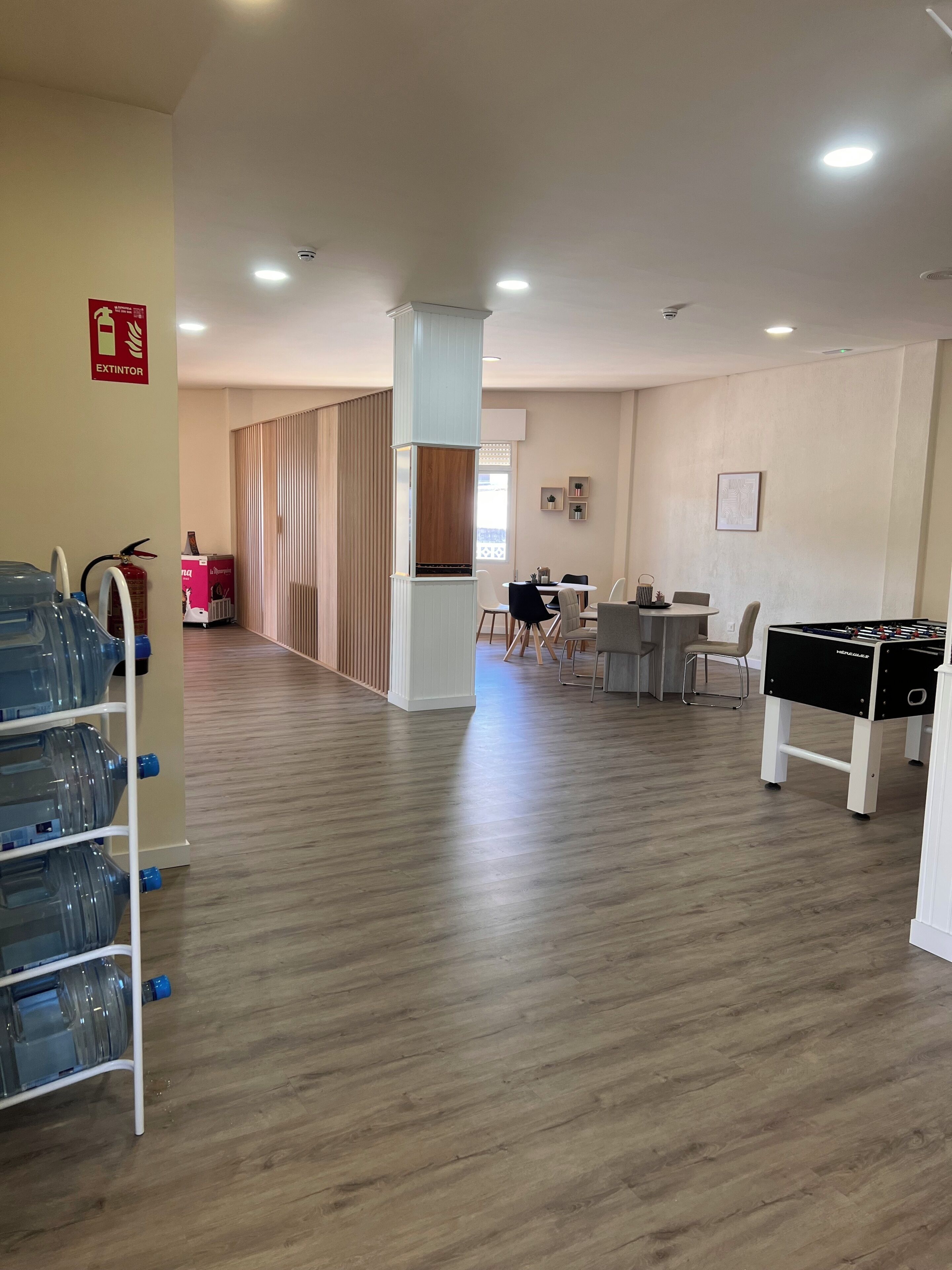 Un hall d’hôtel équipé d’un distributeur d’eau, d’un extincteur, d’un baby-foot et d’un espace repas avec des chaises et une table.