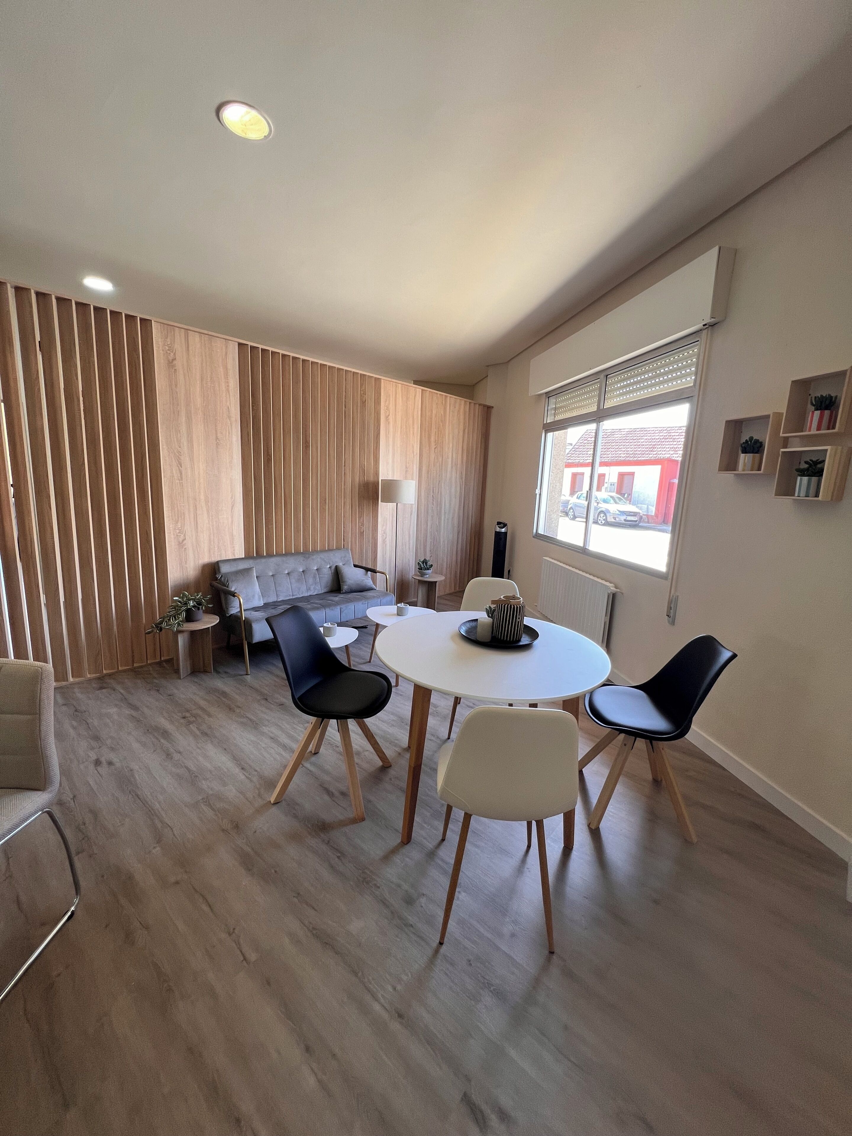 A modern living room with a sofa, a dining table with chairs, and a large window with a view of the outside.