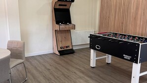 Una habitación con mesa de fútbol de mesa y una máquina de videojuegos de madera con el rótulo 'GLINT'.