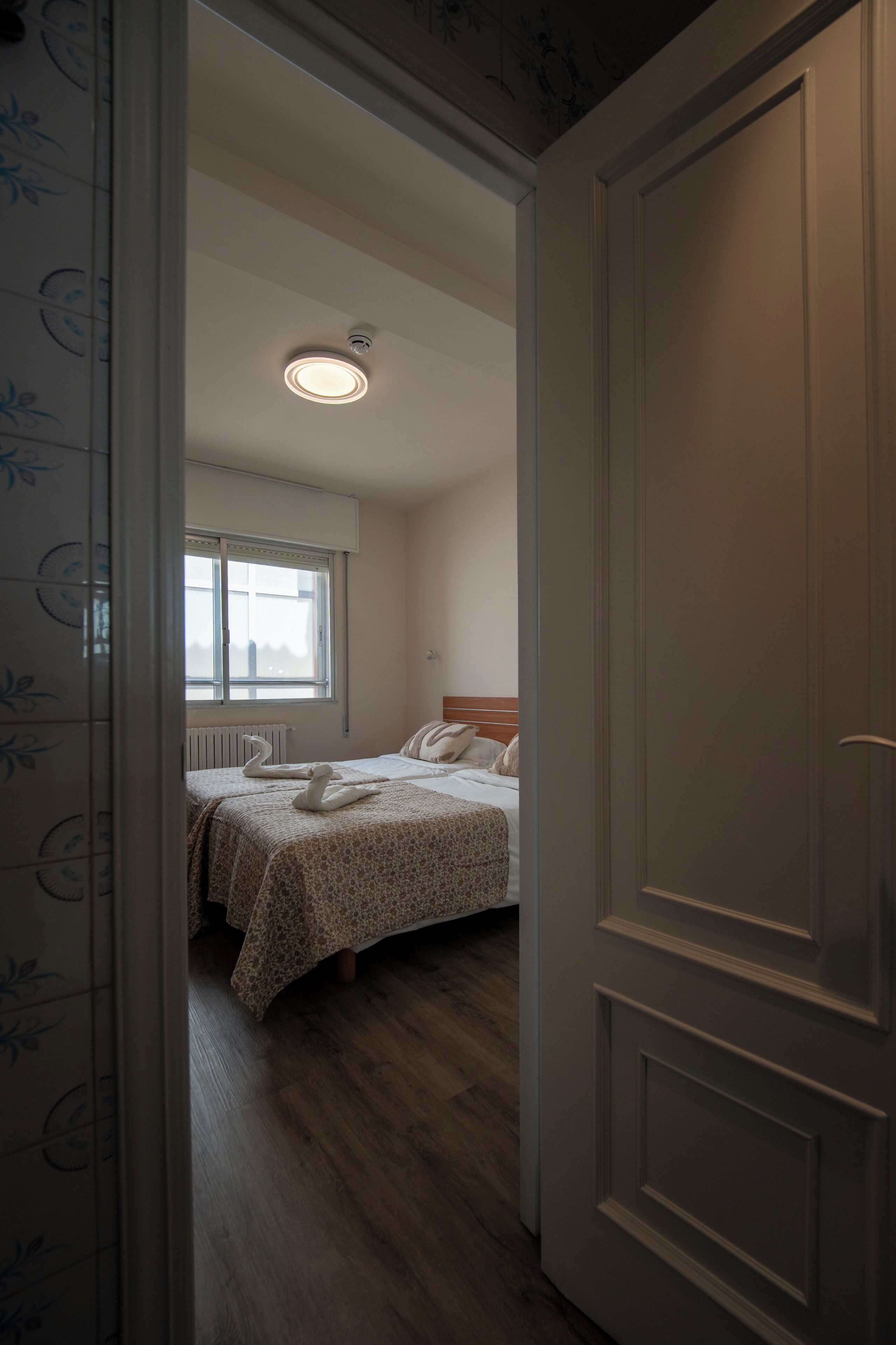 Una habitación de hotel con una cama, ventana, radiador y puerta.