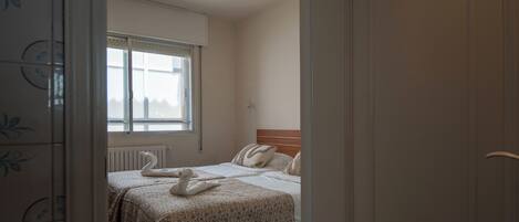 A hotel room with a bed, a window, a radiator, and a door.
