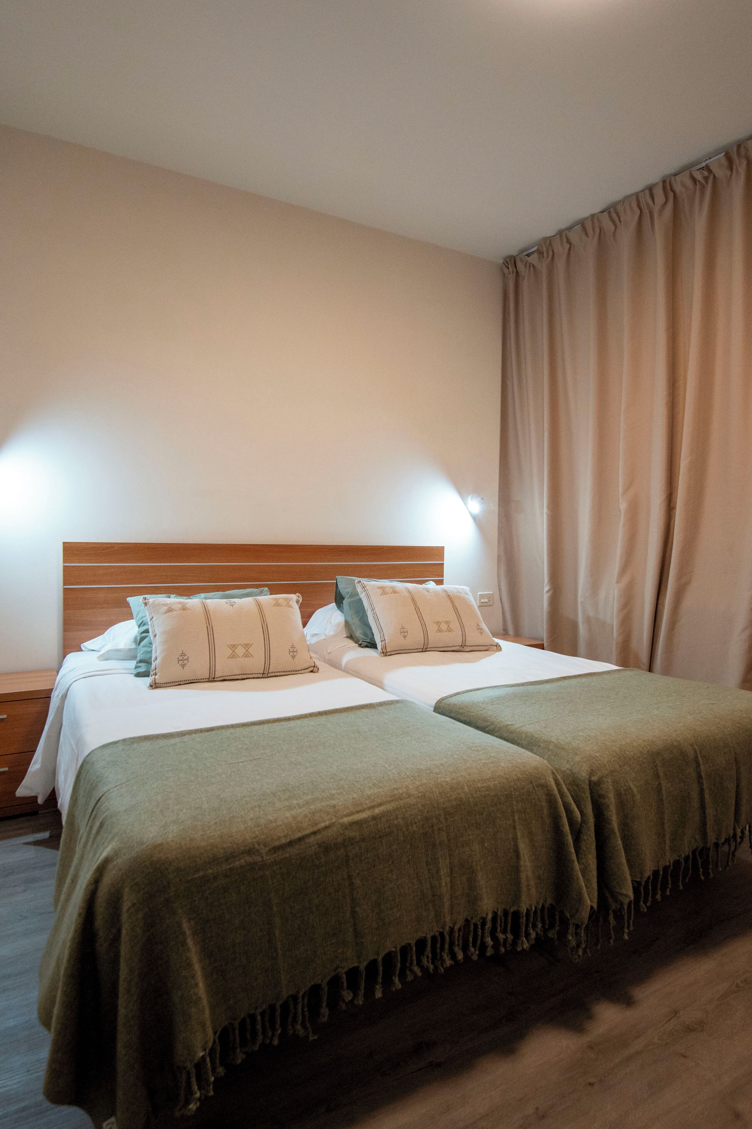 Een tweepersoonsbed met twee kussens, een houten hoofdbord en een nachtkastje met een lamp.