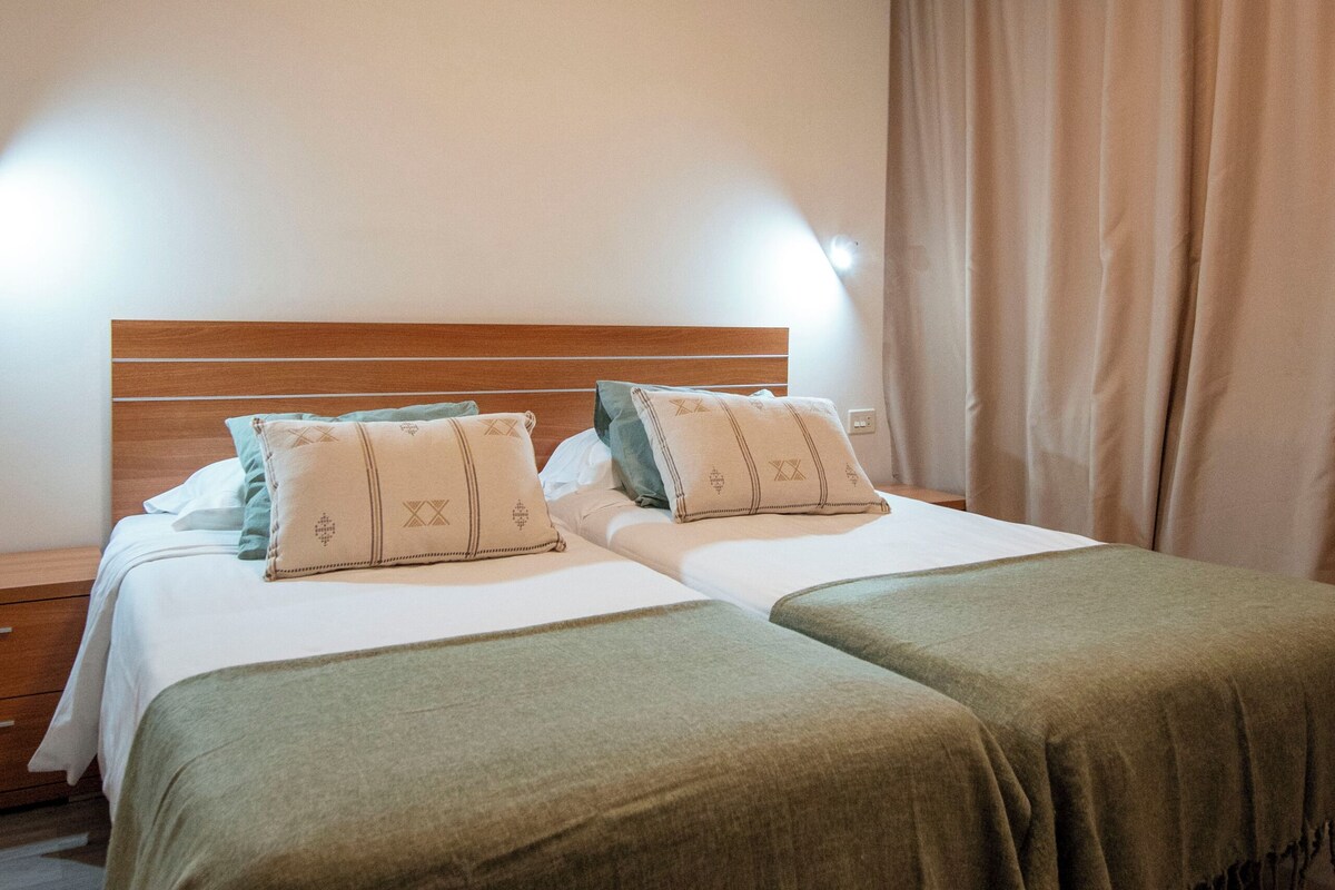 A double bed with two pillows, a wooden headboard, and a nightstand with a lamp.