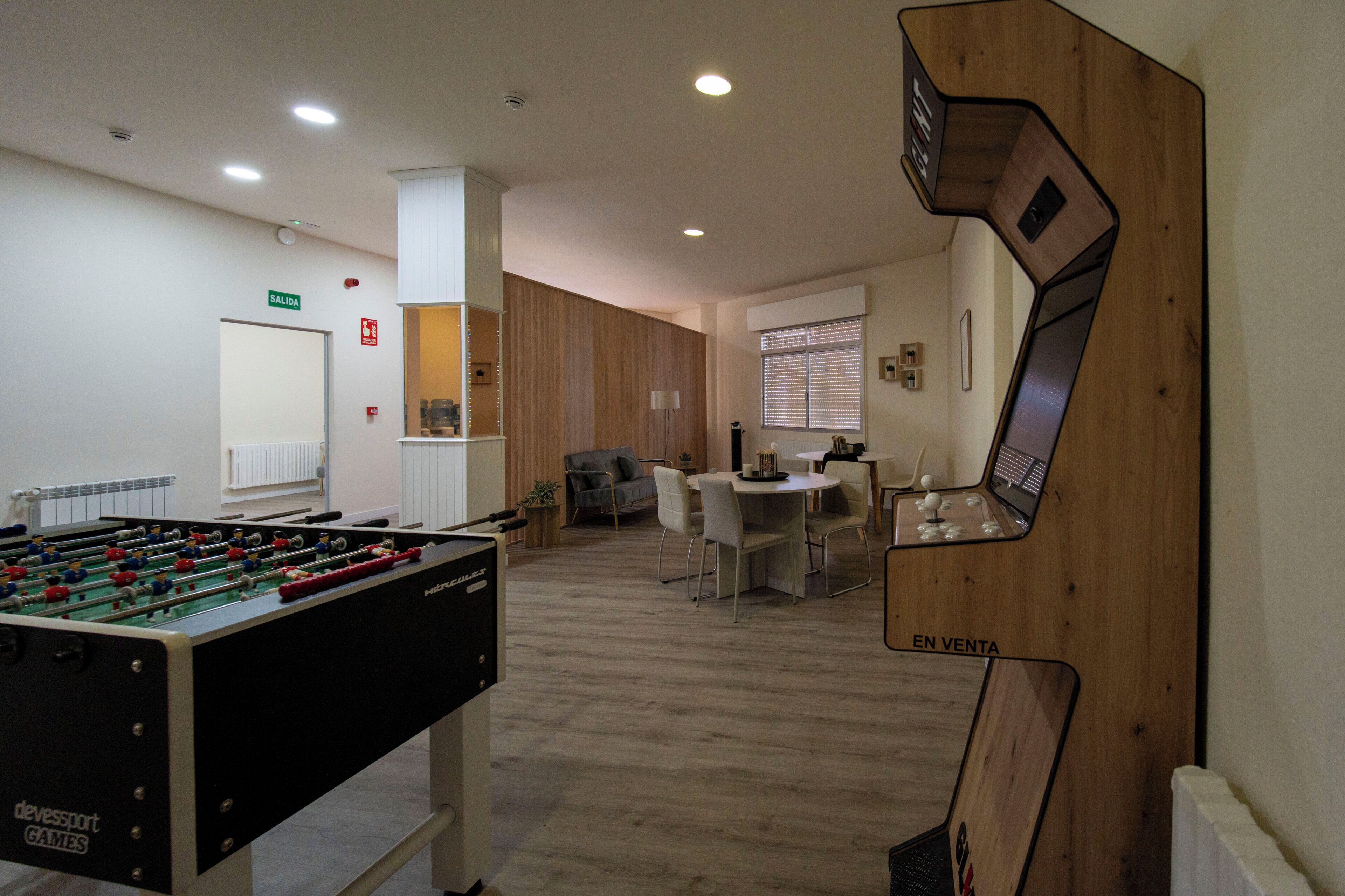 Habitación con mesa de fútbol, zona de comedor con mesa y sillas, y una pantalla de televisión montada en la pared.