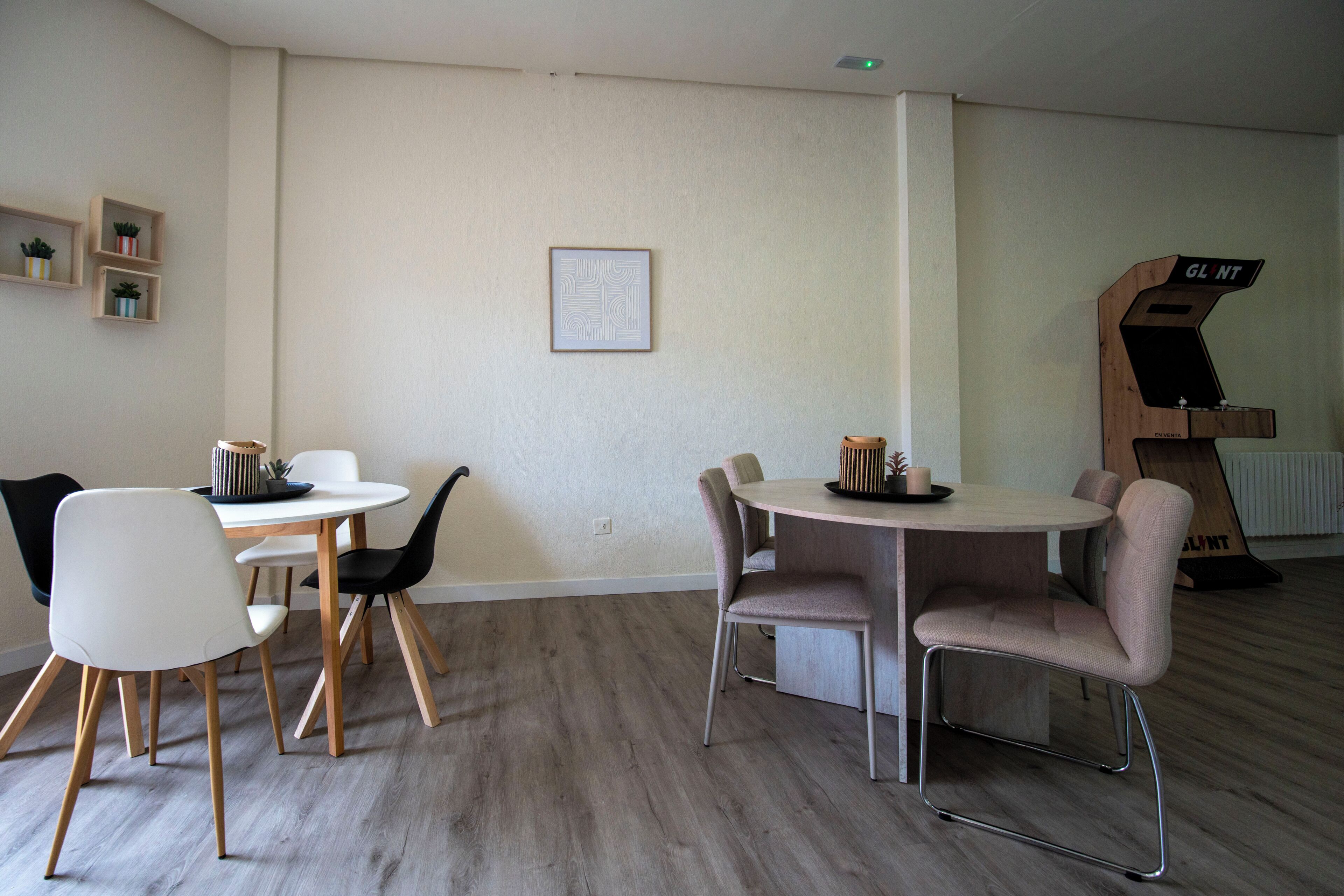 Una habitación con dos mesas redondas, sillas, un armario de madera y un cuadro en la pared.