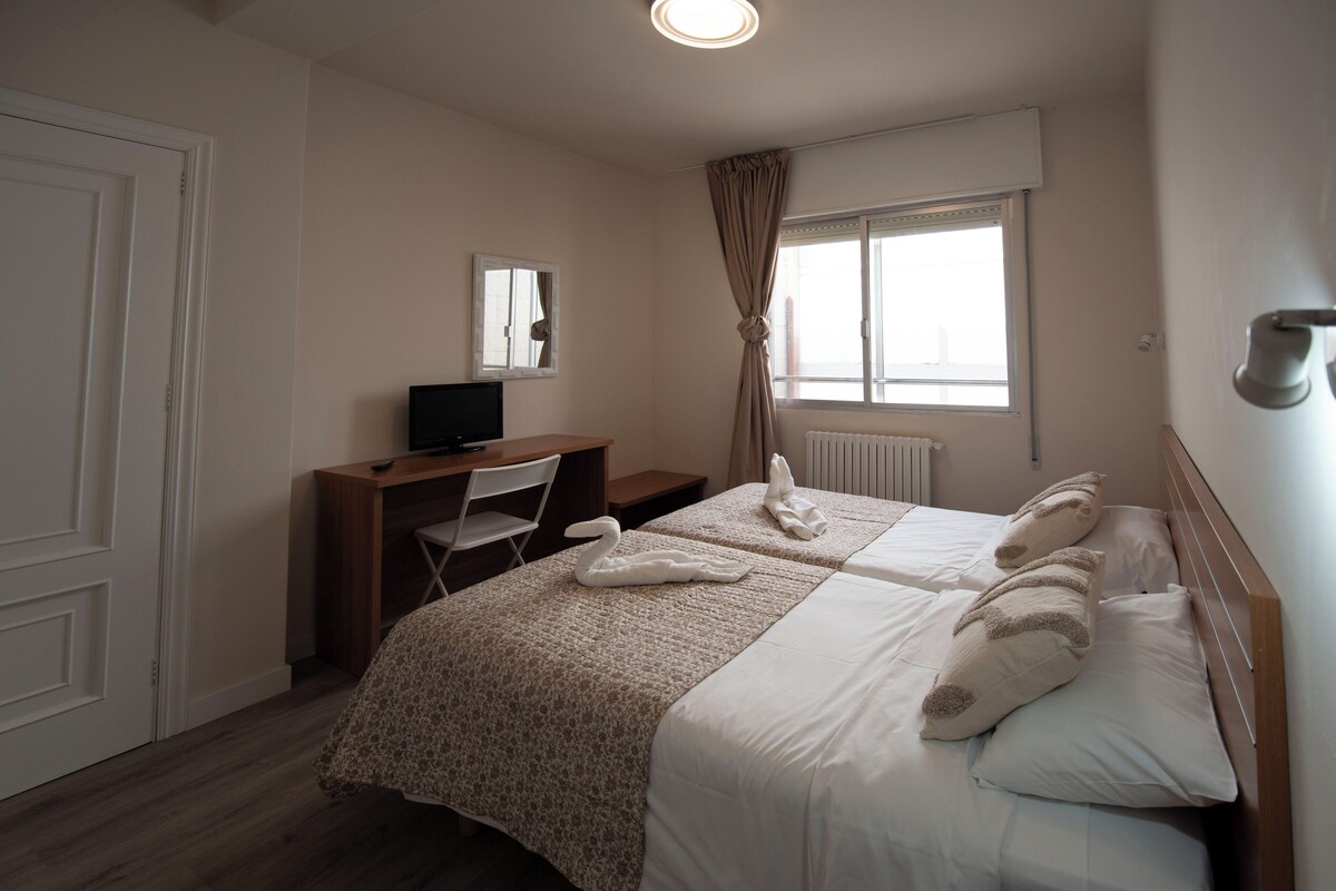 Een hotelkamer met twee bedden, een bureau met stoel, een televisie en een raam met gordijnen.