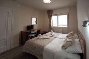 Habitación de hotel con dos camas, un escritorio con silla, televisión y ventana con cortinas.