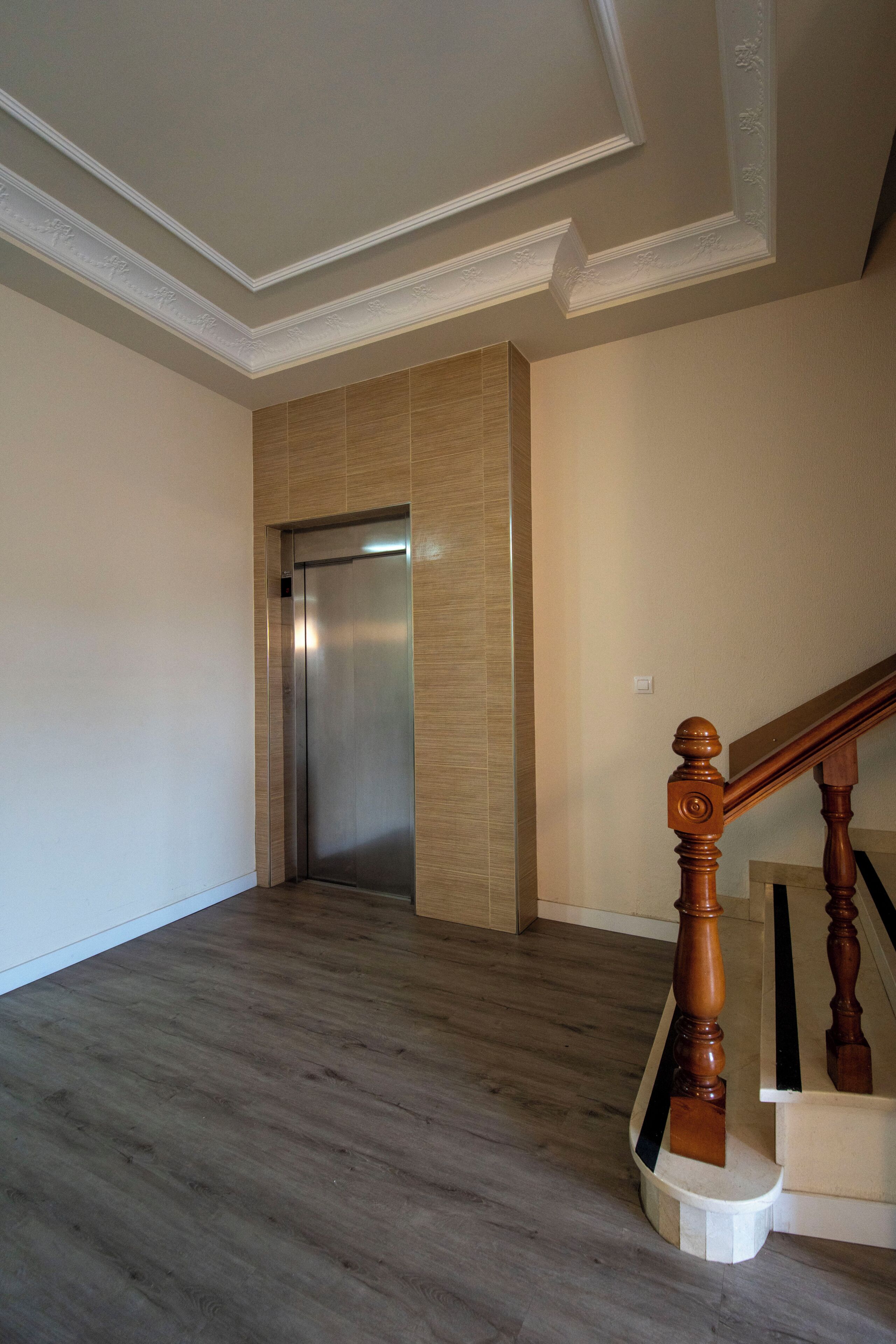 Un interior espacioso con una escalera de madera, un ascensor moderno y una pared lisa.