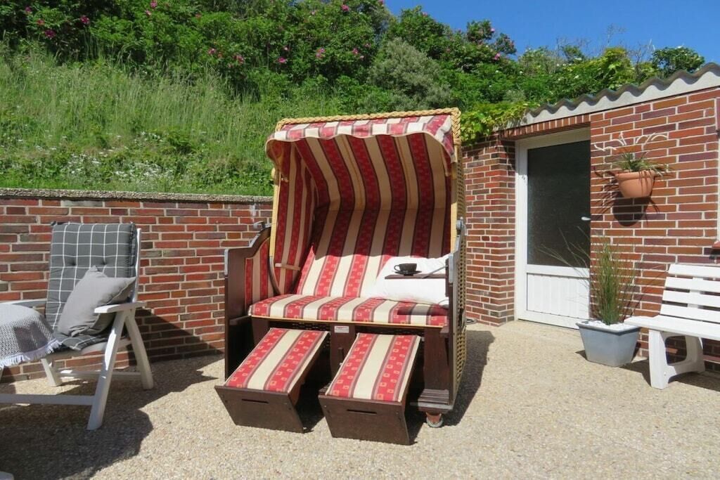 A sunlit outdoor seating area with a striped canopy chair, a cushioned bench, and a potted plant.