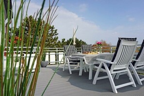 A deck with white chairs and a table, surrounded by a white fence and greenery. - Amber in the House Sea Greeting (Juist)