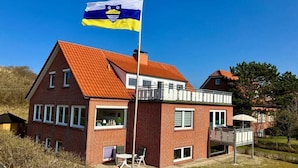 Et toetages murhus med rødt tag, en balkon og et flagstang med flag.