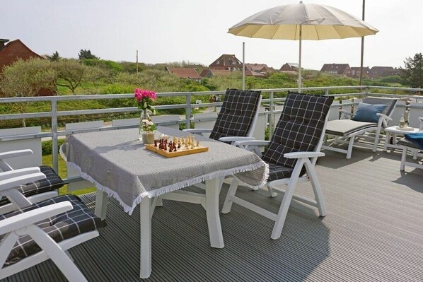 A deck with a chessboard, chairs, and a table with a cloth. - Amber in the House Sea Greeting (Juist)