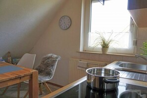 A kitchen with a clock on the wall, a window with a plant, and a chair. - Amber in the House Sea Greeting (Juist)