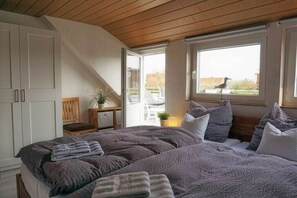 A bedroom with a large bed, a window with a view, and a door leading to an outdoor area. - Amber in the House Sea Greeting (Juist)