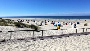 En strand med en træpromenade der fører ned til sanden, samt flere farverige strandparasoller og liggestole.