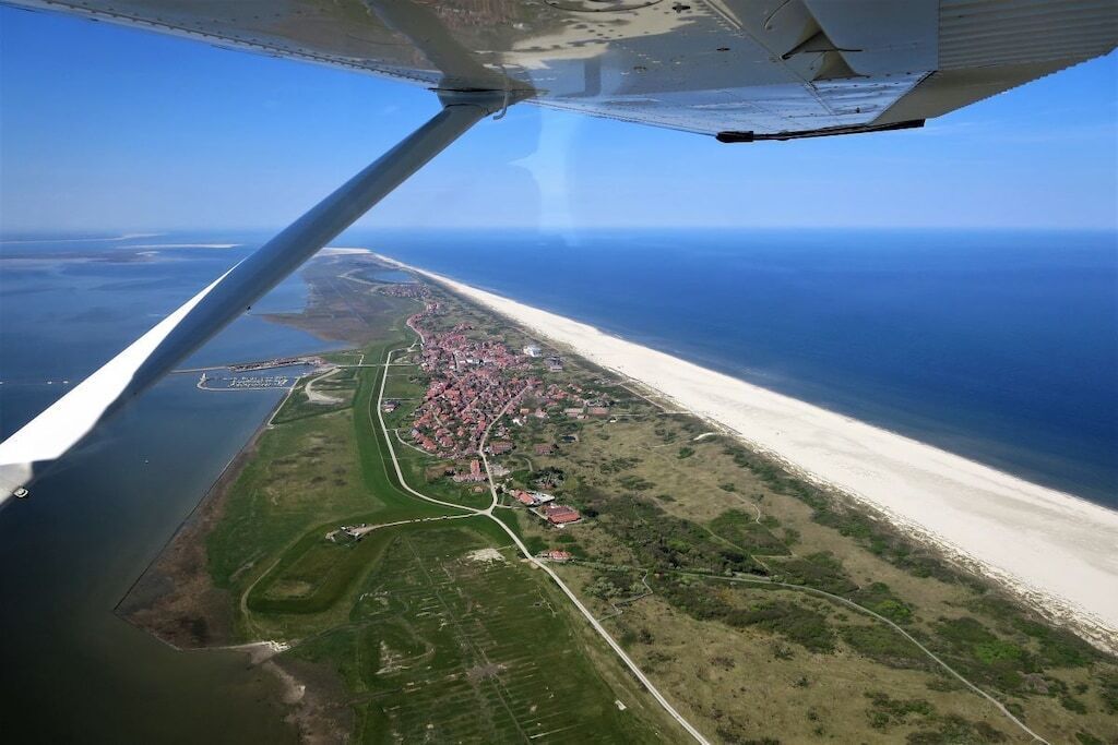 Eine Luftaufnahme einer Küstenregion mit Strand, einer kleinen Stadt und einem Gewässer.