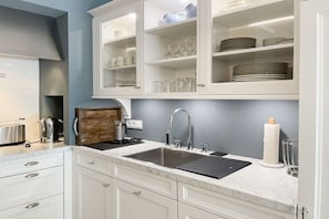 A kitchen with white cabinets, a double sink, and a countertop with a kettle and toaster. - Penthouse Maison Plage (Scharbeutz)