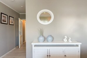A hallway with a white console table, two vases, a mirror, and framed pictures on the wall. - Penthouse Maison Plage (Scharbeutz)