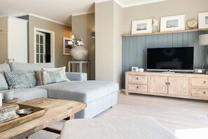 A modern living room with a grey sofa, wooden coffee table, and a television on a wooden cabinet. - Penthouse Maison Plage (Scharbeutz)