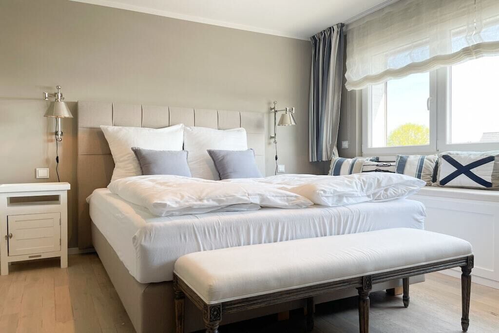 A bedroom with a bed, bedside tables, a bench, and a window with curtains.