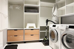 A laundry area with a washing machine, a vacuum cleaner, and storage drawers. - Penthouse Maison Plage (Scharbeutz)