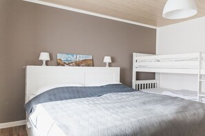 Une chambre avec un lit superposé, un lit recouvert d’une couvre-lit à motifs, deux lampes de chevet et un tableau accroché au mur.
