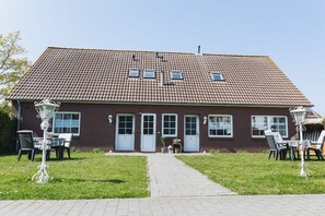 En toetages murbygning med et tegltag, en midterindgang med dobbelte døre, og en belagt sti, der fører til indgangen.
